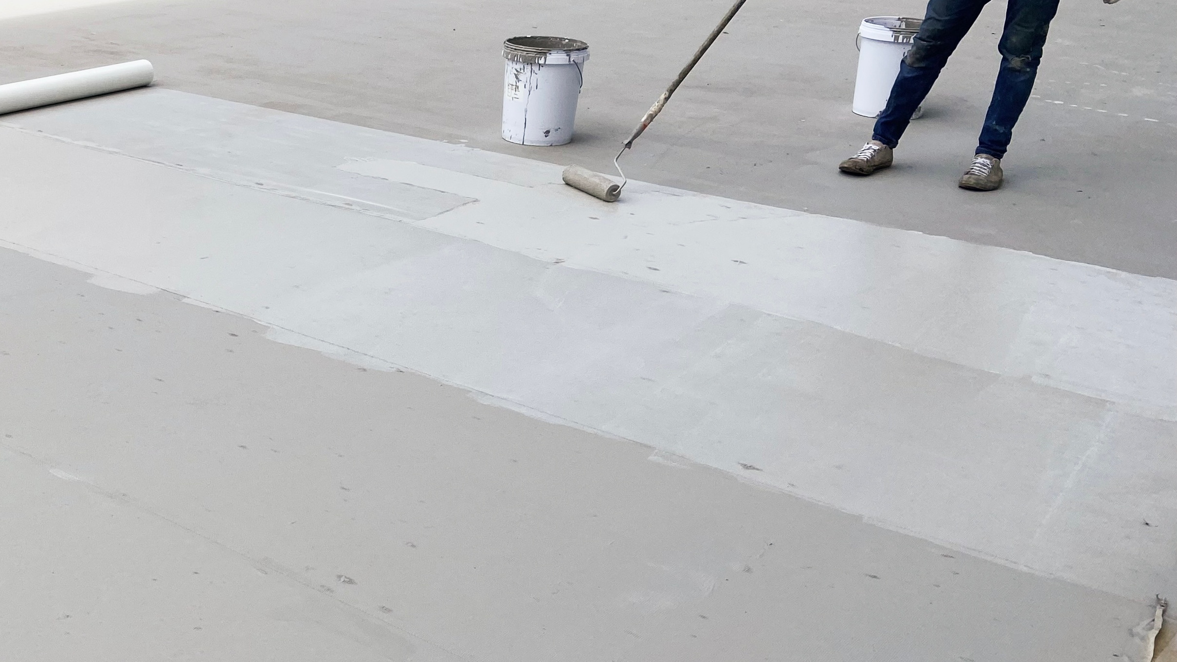 A commercial roofing restoration contractor applying a waterproof membrane to a flat roof